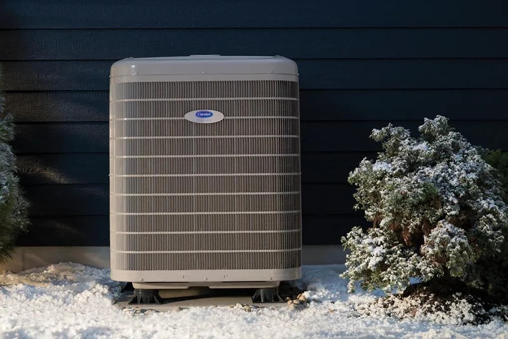 Carrier Infinity heat pump installed against dark siding with snow on the ground