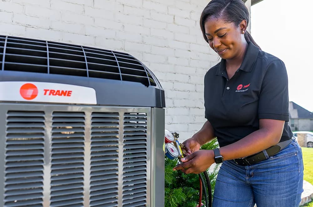 Trane technician checking refrigerant gauges on an outdoor heat pump unit